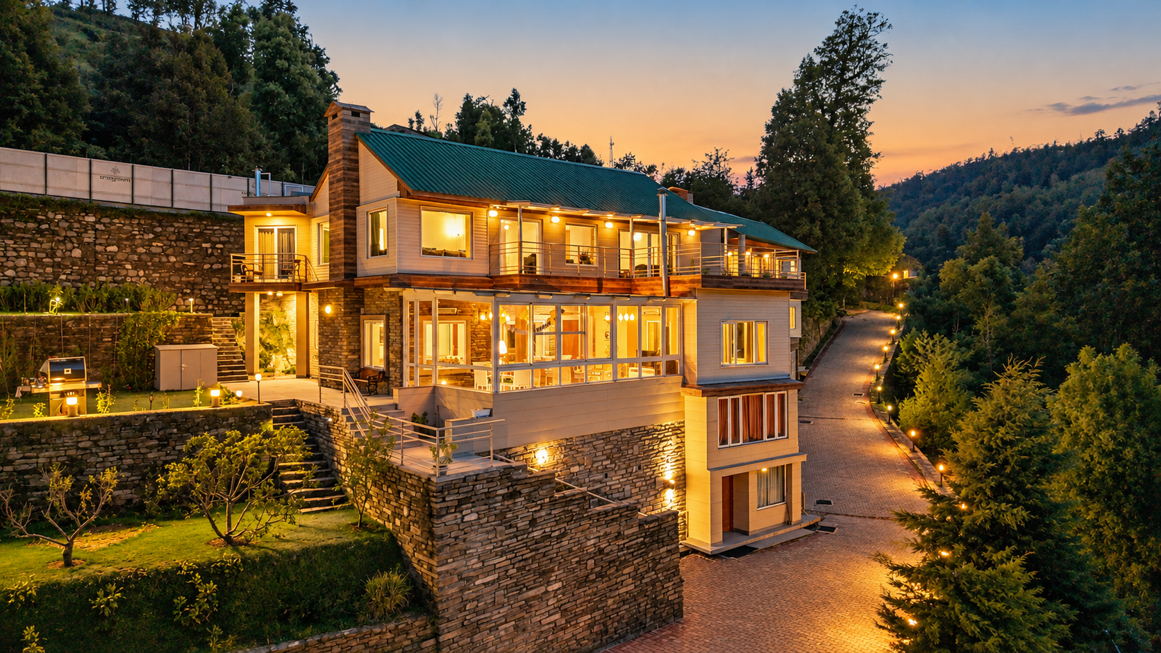 Luxury hillside villa with warm lighting, stone walls, spacious balconies, and a landscaped garden at sunset.